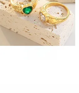 Close-up of golden oval rings featuring heart-shaped emerald and clear gemstones