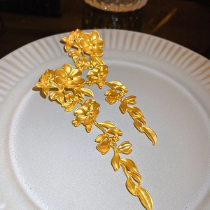 Detailed shot of golden flower and leaf tassel earrings on white ceramic plate