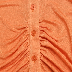 Detail of orange shimmer knit shirt featuring matching buttons and ruched front design