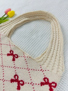 Detail of cream knit tote bag with red bow patterns and textured woven handles