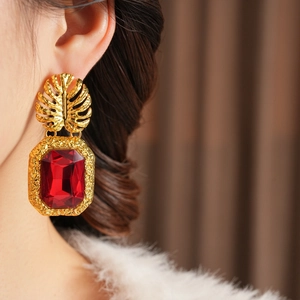 Détail de boucles d'oreilles feuille dorée avec gemme rouge sur un mannequin femme