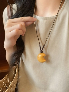 Detailed view of handcrafted moon-shaped wooden pendant necklace on a woven cord strap