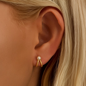 Close-up of elegant C-shaped gold pearl earrings on model with polished finish