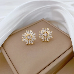 Macro view of gold snowflake earrings with sparkling zircons on soft white silk fabric