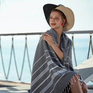 Dark gray Turkish beach towel with white stripes and fringe, worn by a model at the seaside