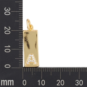 Golden rectangular pendant with zircon letter A being measured on a black scale ruler