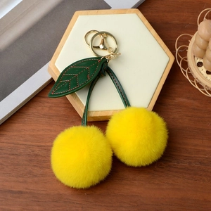 Detail of yellow cherry plush keychain with green leather leaf and gold metal clasp