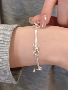 Detail of silver bow bracelet on wrist featuring a sleek flat snake chain design