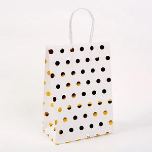 Close-up of white kraft paper gift bag with golden polka dots and twisted rope handles