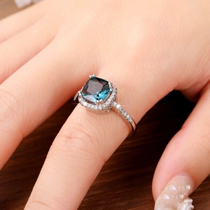 Close-up of cushion-cut blue gemstone ring with halo setting on a model hand