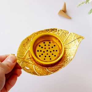 Elegant gold leaf-shaped metal incense holder with detailed texture on white surface