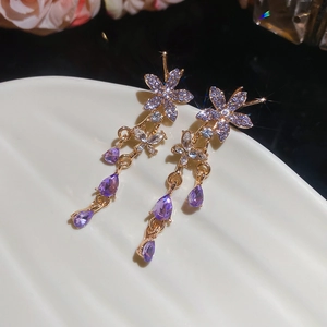 Detail of elegant gold earrings with purple flower and drop-shaped crystal on white plate