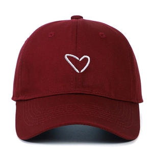 Detail of burgundy cotton baseball cap featuring white heart embroidery on a curved brim