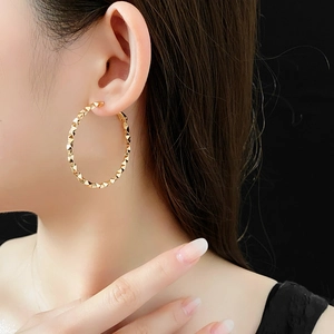 Primo piano di modella che indossa grandi orecchini a cerchio dorati con design sfaccettato