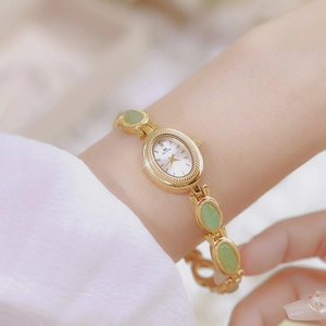 Elegant gold chain watch with green jade stones on female wrist, oval white dial
