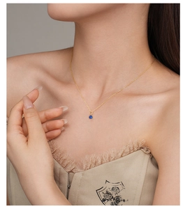 Detail of s925 silver gold-plated necklace with a round blue gemstone on collarbone
