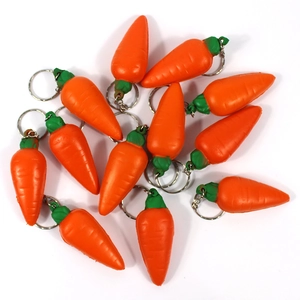 Flat lay of multiple orange carrot keychains with green leaves on white background