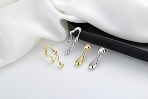 Detail view of liquid metal gold and silver stud earrings on a white satin cloth