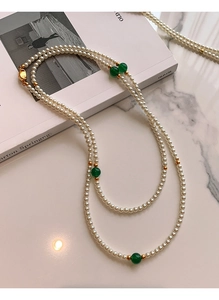 Elegant pearl necklace with green beads and gold spacers on white marble surface