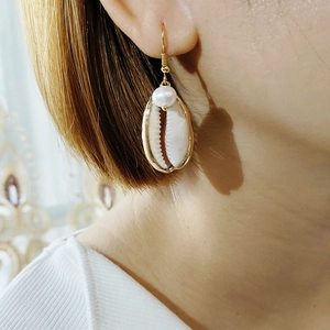 Detail showing the golden conch shell earring with a white pearl on the ear