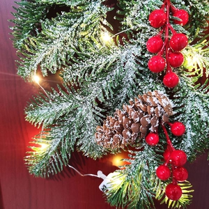 Close-up of snowy Christmas pine branch with red berries, pinecones and warm LED lights