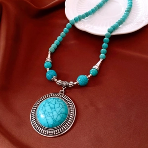 Close-up of vintage turquoise beaded necklace with engraved silver disc on red silk