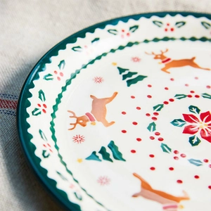 Detail of hand-painted ceramic plate with orange reindeer and green Christmas tree motifs