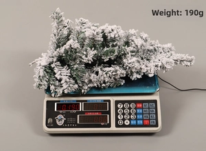 Detail shot of a 190g artificial snow-flocked pine branch shown on a digital weight scale