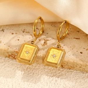 Détail de boucles d'oreilles pendantes dorées avec gravure d'étoile et petit zircon