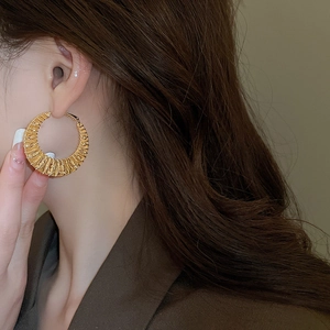 Detailed close-up of large gold twisted hoop earrings with textured spiral design