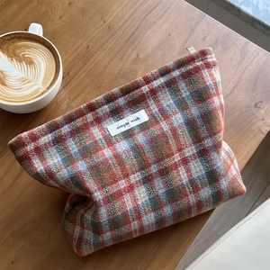 Detail of multi-color plaid tweed makeup bag on a wooden table with coffee