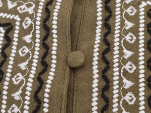 Détail macro de la chemise en lin vert olive avec broderie géométrique et bouton en tissu
