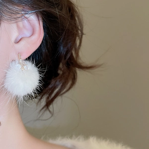 Close-up of a plush white pom-pom earring with zircon accents worn by a model