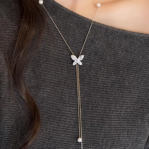 Detail of zircon butterfly necklace with white pearls worn on a grey knit top