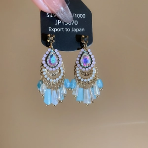 Macro detail of fan-shaped tassel earrings with iridescent gems and blue beads