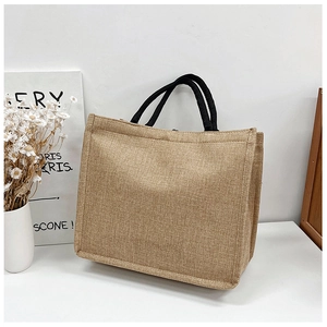 Close-up of a brown jute tote bag with black rope handles beside a decorative vase