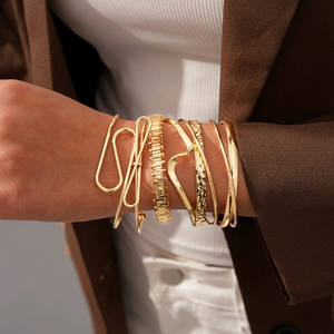 Détail d'un ensemble de 6 bracelets dorés superposés, géométriques et torsadés au poignet