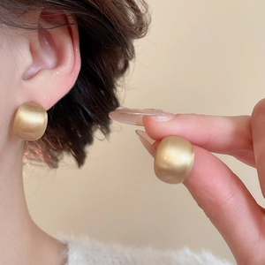 Detail of matte gold dome earrings featuring a luxury brushed texture on broad metal bands