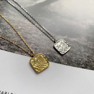 Macro detail of textured square pendant necklace featuring embossed fern leaf design