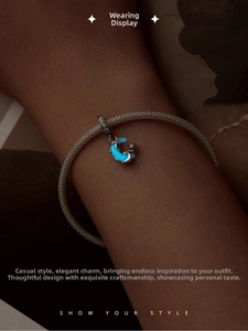 Glow-in-the-dark moon and cat charm on a silver mesh bracelet under dim lighting