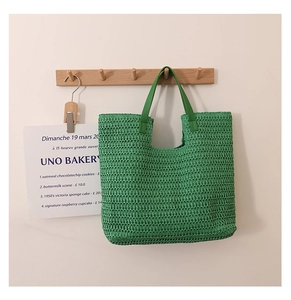 Detailed texture of green woven straw tote bag hanging on a minimalist wooden hook