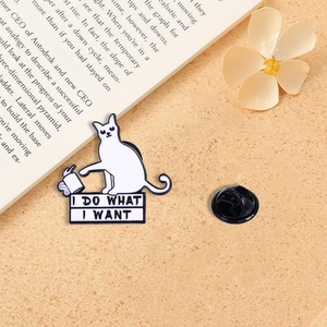 Detail der Emaille-Anstecknadel Katze mit Spruch auf einem warmen Schreibtischhintergrund