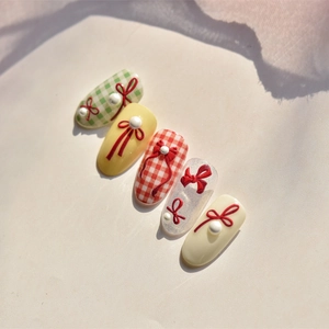 Detail of five press-on nails featuring red 3D bows and pearls on textured beige background