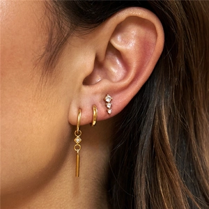 Close-up of gold flower diamond stackable earring set worn on ear with zircon pendants