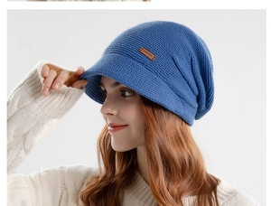 Gedetailleerde gebreide textuur van een blauwe wintermuts met een leren merklogo patch