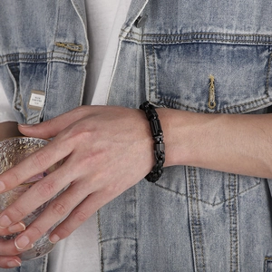Close-up of men's black stainless steel chain bracelet worn while holding a glass