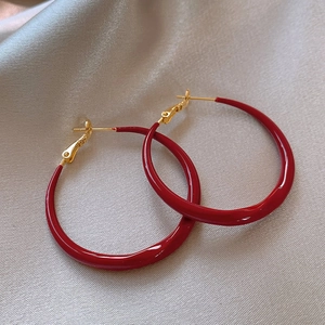Detail shot of red C-shape plush enamel earrings on silk background with gold posts
