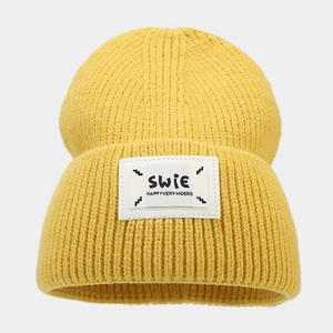 Detailed view of yellow ribbed knit beanie featuring a white lettered patch on the folded cuff