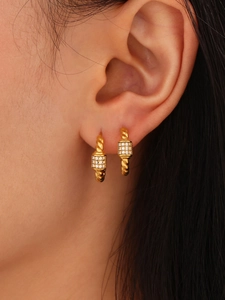 Close-up of gold twist C-hoop earrings with zircon square detail in a layered style