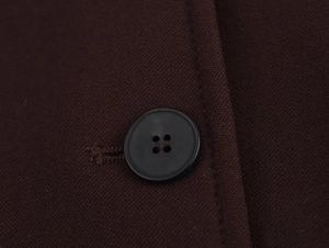 Detailaufnahme eines matten schwarzen Knopfes auf kaffeebraunem Webstoff des Blazers